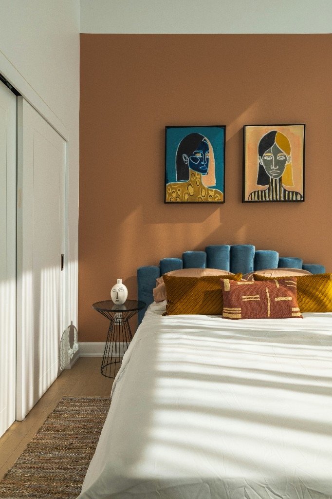 Bedroom with blue velvet headboard, terracotta wall, and curated furniture